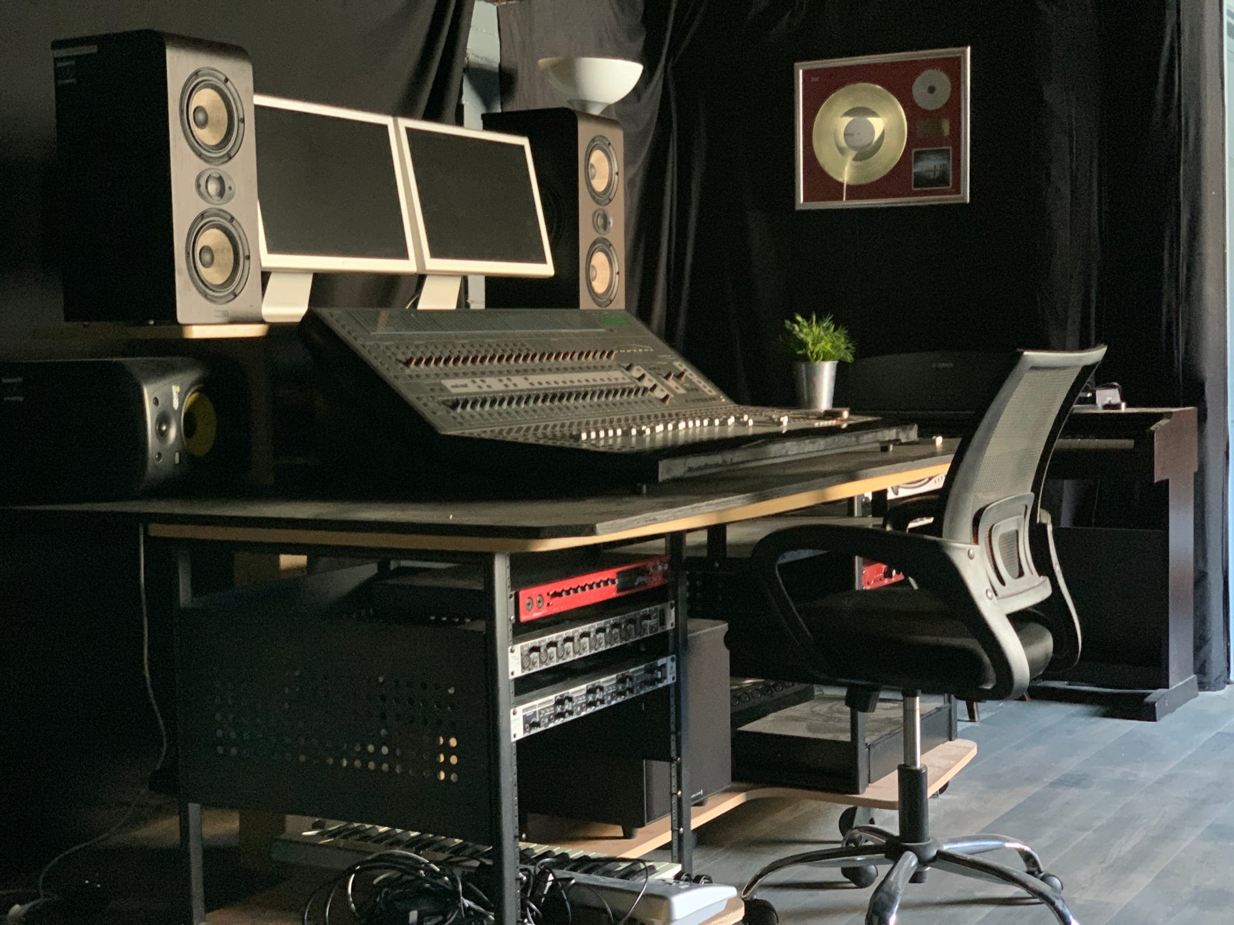 Control room desk and monitors with a framed gold disc on the wall